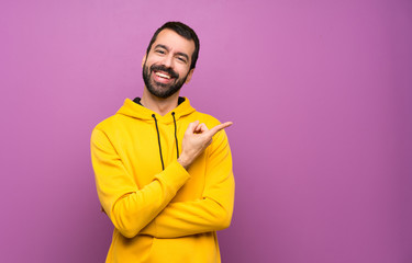 Obraz premium Handsome man with yellow sweatshirt pointing to the side to present a product