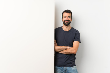 Young handsome man with beard holding a big empty placard keeping the arms crossed in frontal position