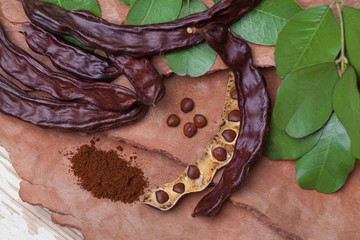 Carob. Organic carob pods with seeds and leaves on tree bark table. Healthy eating, food background.