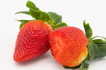 Cluster of organically grown and ripe Strawberries, showing one of the large Strawberries with a bite taken out of it. Shown together with there great leaves as seen on a plate.