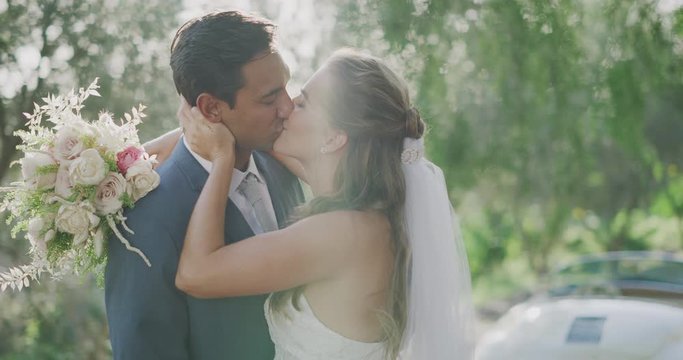 Happy diverse couple about to get married smiling and embracing to kiss in the afternoon sun rays on a country road with green trees, the perfect wedding day