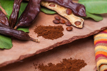 Carob. Organic carob pods with seeds and leaves on tree bark table. Healthy eating, food background.