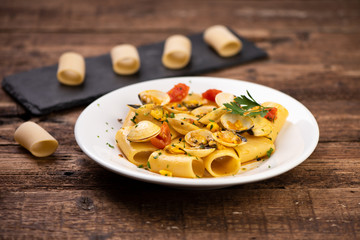 Paccheri pasta with clams on white plate on rustic table.