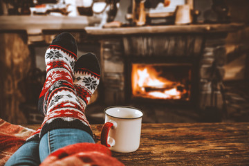 Legs in winter christmas socks on wooden top board with fireplace background in cozy home interior.