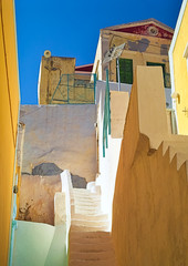 Stairs between houses in Symi island, Greece. Yellow paint contrasts with deep blue sky.