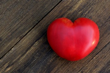Obraz na płótnie Canvas Bright red heart shaped tomato on wooden background close up
