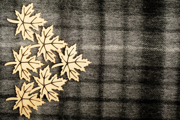Six light brown wooden leaves on black and grey textured textile wool material background with vertical and horizontal stripes, on left side with space for text, top view with laser cut wooden objects