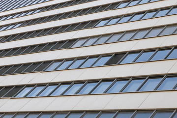 Ground view of high modern building with many windows and blue sky reflection on it