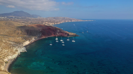 Aerial drone photo of iconic famous red rocky volcanic beach with deep turquoise sea visited by sail boats, Santorini island, Cyclades, Greece