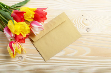 Colorful tulips and blank envelope on natural wooden background with space for text