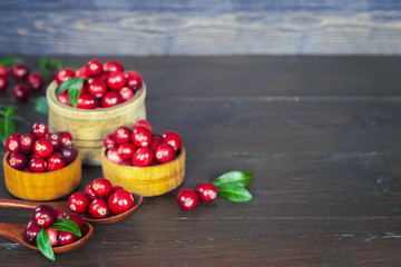 Obraz na płótnie Canvas fresh cranberries in wooden bowls and wooden spoons closeup. ripe cranberries on a wooden background. cranberries and leaves close-up.