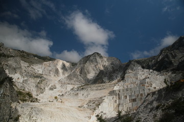 Panorama of a white Carrara marble quarry in Tuscany. Mountains of the Apuan Alps, blue sky and cloud.