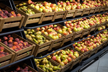 Supermarket counter with wooden lug boxes full with fruit: apples, pears and peaches