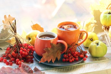 Two cups of tea, fruits, berries, leaves on a wooden table on a window background, romantic autumn composition, home comfort concept, healthy food