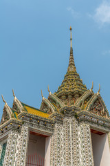 Fototapeta premium Bangkok city, Thailand - March 17, 2019: Gables and greenish spire of smaller section of Temple of Dawn, with its colorful porcelain faience surface, golden roof, against blue sky.