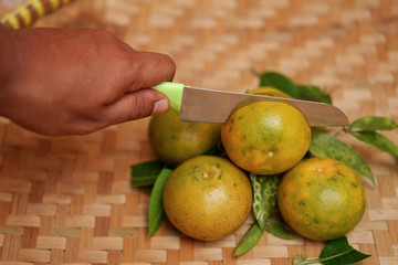 Hand holding a knife cutting fresh oranges on rattan bamboo woven. 