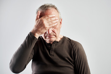 elderly gray-haired man with expression of pain on face put his hand on head, feels dizzy and...