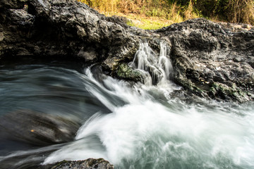 CLOSE UP: Foaming river water flows down large black rocks in the middle of a tropical forest