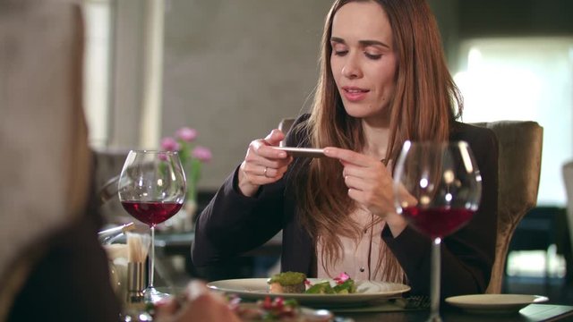 Businesswoman taking food photo on smartphone at restaurant