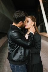 A man in a black leather jacket and a woman in a black jacket, hugging standing. A man wants to kiss a woman passionately.