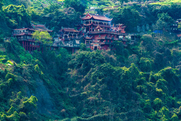 The ancient Taoist monastery in China on the side of the mountain among the forest and bushes. Chinese city of Chongqing.