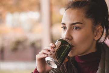 Brunette girl in a sweater in a cafe on the street in the autumn in a thoughtful mood drinks from a can.