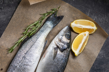 Fresh fish seabass and ingredients for cooking, lemon and rosemary. Dark background top view.