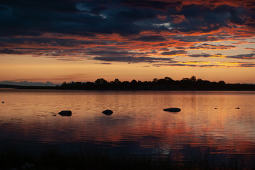 Naklejka premium Orange and red sky and dark blue clouds over a quiet lake at sunrise