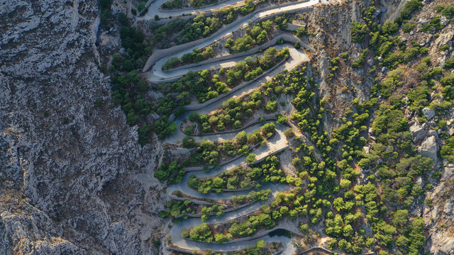 Aerial drone photo of snake narrow road leading to archaeological site of ancient Thera or Thira built uphill, Santorini island, Cyclades, Greece