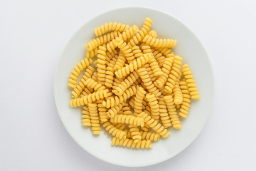 Group of dried fusilli Italian pasta on a white plate ready to be cooked, isolated on white table, with view from above 