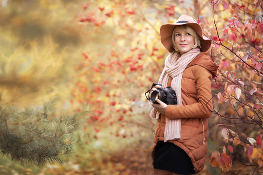 young woman in a hat photographs outdoors in autumn