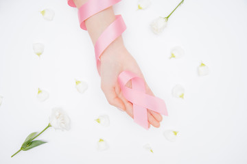 Girl hands holding pink breast cancer awareness ribbon on white background with flowers. Concept healthcare and medicine beauty care skin. Top view