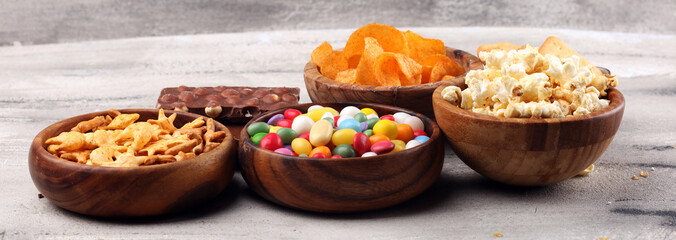 Salty snacks. Pretzels, chips, crackers in wooden bowls and candy and chocolate on table