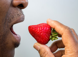 Obraz premium close up of a ripe fresh strawberry at the open mouth of an African American man