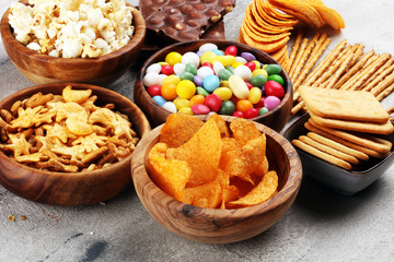 Salty snacks. Pretzels, chips, crackers in wooden bowls and candy and chocolate on table