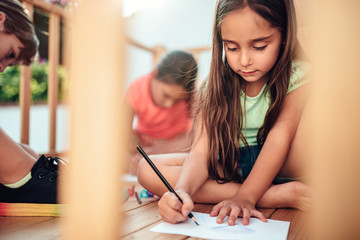 Girl playing in treehouse with friends and drawing with colored pencils