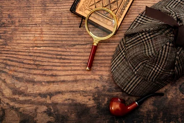 Muurstickers Literary fiction, investigate crime and mystery story conceptual idea with sherlock holmes detective hat, smoking pipe, retro magnifying glass and old book isolated on wood table top with copy space © Victor Moussa