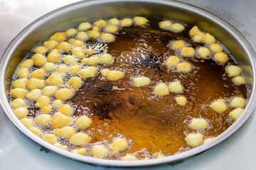 Small donuts being deep fried in boiling oil in a large pan, at a street food market, selective focus