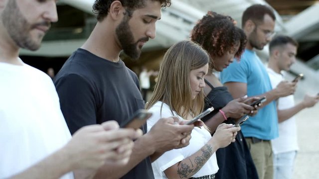 Pensive young friends using smartphones on street. Thoughtful young people standing in row and using digital devices. Technology concept