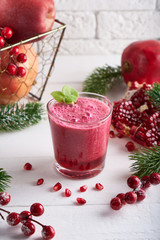 pomegranate smoothie in a glass on a white wooden table with fir branches and winter berries Close up