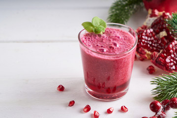 pomegranate smoothie in a glass on a white wooden table with fir branches and winter berries Copyspace