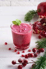 pomegranate smoothie in a glass on a white wooden table with fir branches and winter berries Close-up