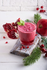 pomegranate smoothie in a glass on a white wooden table with fir branches and winter berries Close-...