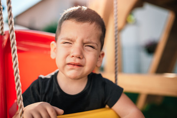 Toddler boy sitting on the swing and whining