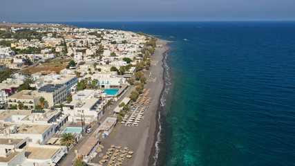 Aerial drone photo of famous seaside village and organised with sun-beds and umbrellas sandy beach of Kamari, Santorini island, Cyclades, Greece