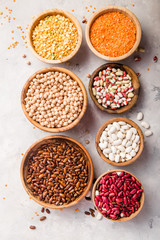 Lentils, chikpea and beans assortment in different bowls on white stone  table top view.