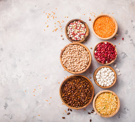 Lentils, chikpea and beans assortment in different bowls on white stone  table top view.
