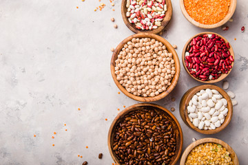 Lentils, chikpea and beans assortment in different bowls on white stone  table top view.