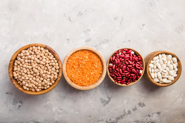 Lentils, chikpea and beans assortment in different bowls on white stone  table top view.