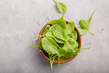 Baby spinach leaves in bowl  on grey concrete background, top view, copy space. Clean eating,...